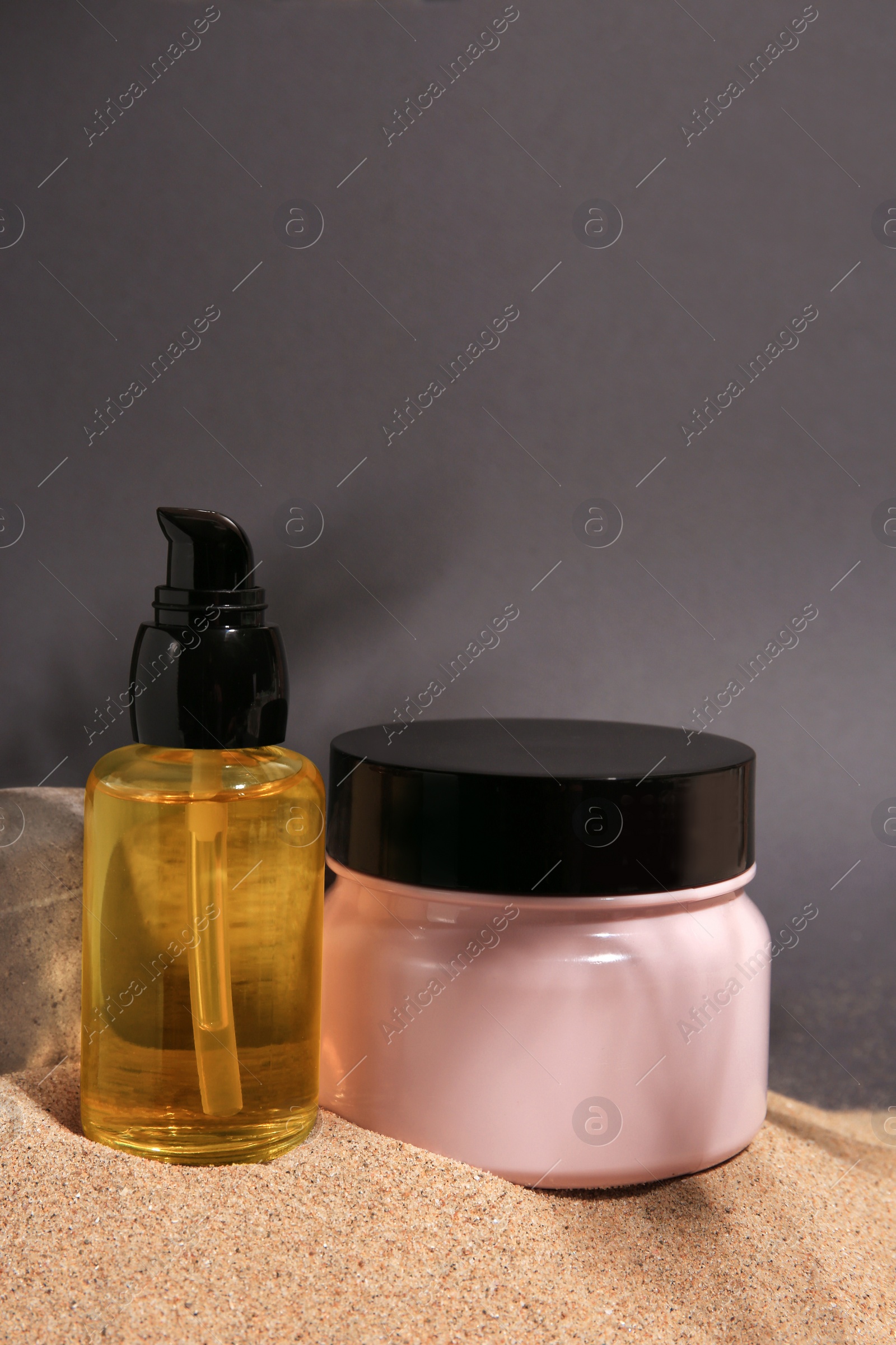 Photo of Cosmetic products and stone on sand against grey background