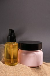 Photo of Cosmetic products and stone on sand against grey background