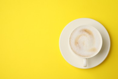 Tasty cappuccino in coffee cup on yellow background, top view. Space for text