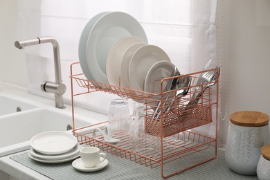 Photo of Drying rack with clean dishes on countertop near sink in kitchen