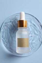Bottle of cosmetic serum on light blue background, top view