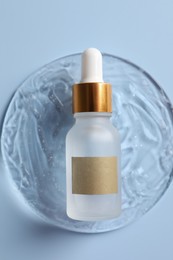 Photo of Bottle of cosmetic serum on light blue background, top view