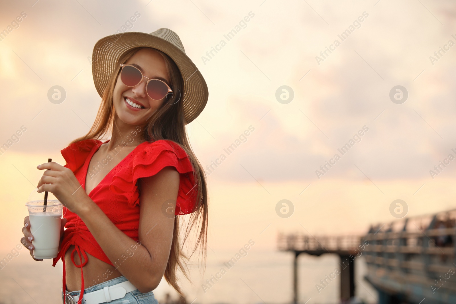 Photo of Beautiful young woman with tasty milk shake outdoors, space for text