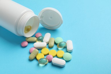 White bottle and different vitamin pills on light blue background, closeup