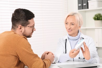 Doctor holding box of pills and consulting patient at white table in clinic