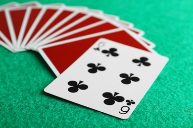 Photo of Playing cards and six of clubs on green table, closeup