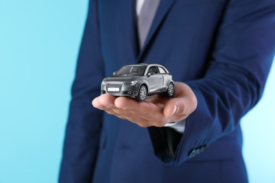 Photo of Insurance agent holding toy car on color background, closeup