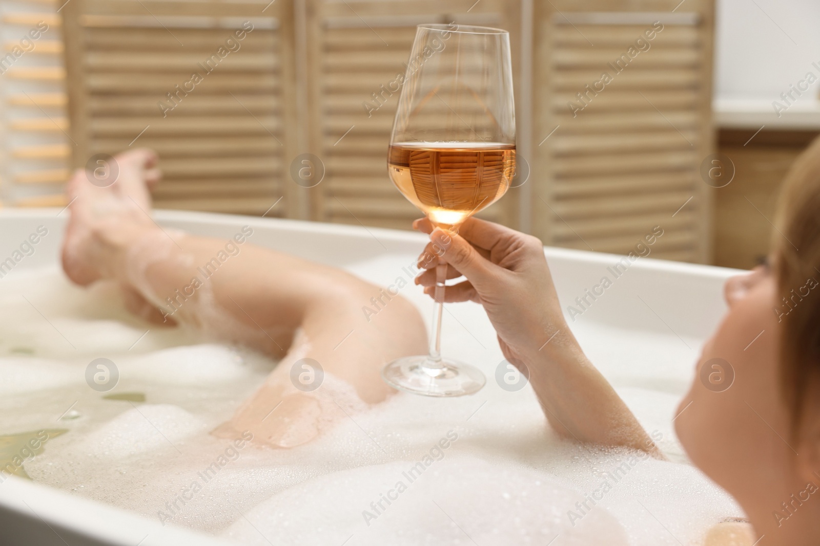 Photo of Woman with glass of wine taking bath in tub indoors, closeup