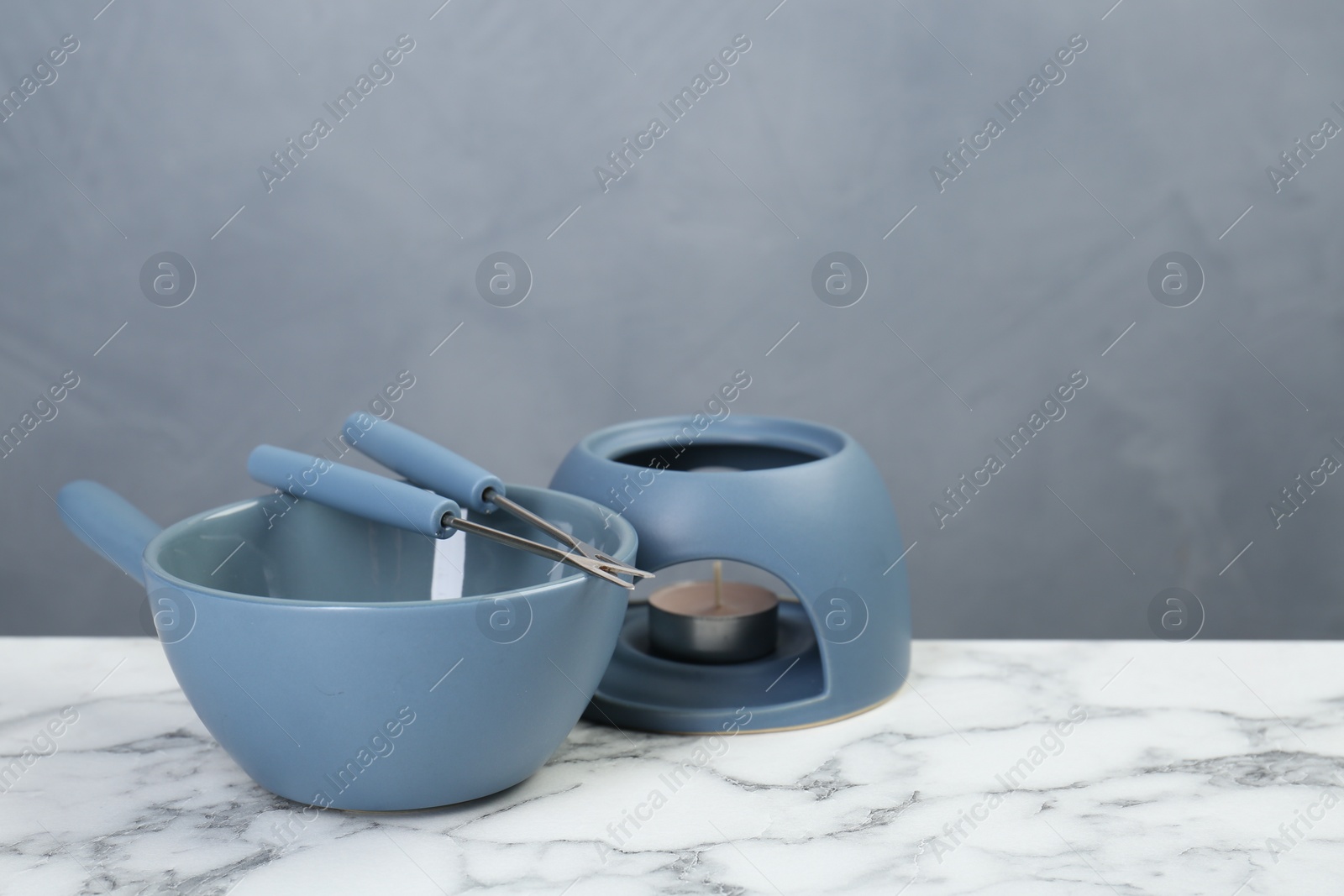 Photo of Fondue set on white marble table against light gray wall, space for text