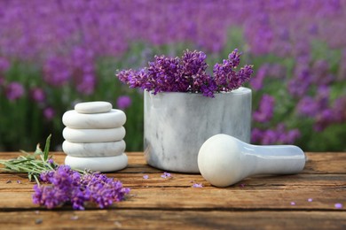 Photo of Spa stones, fresh lavender flowers and white marble mortar on wooden table outdoors, closeup