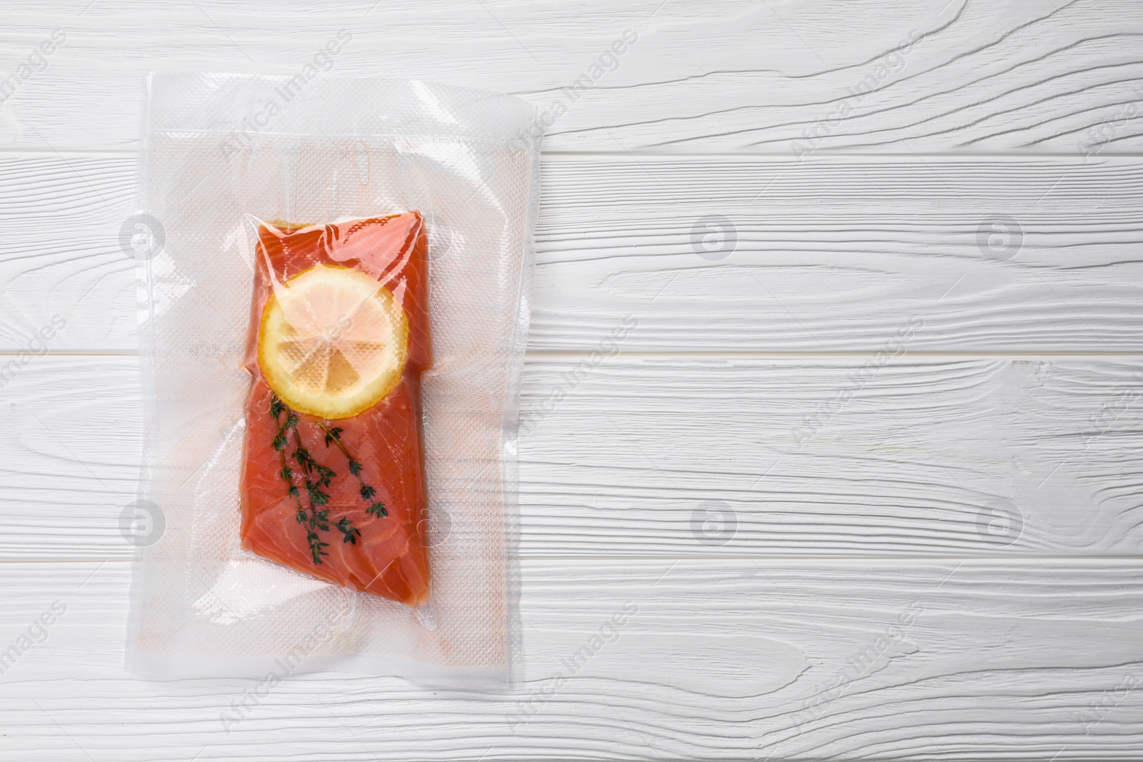 Photo of Vacuum pack of salmon on white wooden table, top view. Space for text