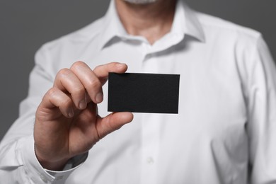 Photo of Man holding blank business card on grey background, closeup