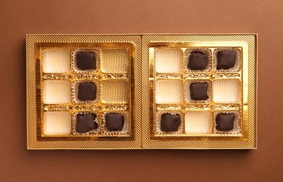 Partially empty box of chocolate candies on brown background, top view