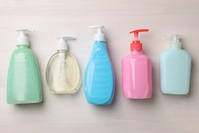 Photo of Many different dispensers of liquid soap on white wooden table, flat lay