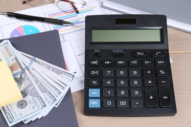 Calculator, dollar banknotes, papers, pen and notebook on wooden table. Pension planning