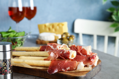 Photo of Tasty prosciutto with breadsticks on grey table