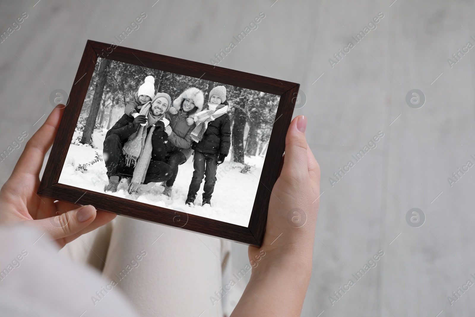 Image of Woman holding frame with black and white photo portrait of her family indoors, closeup