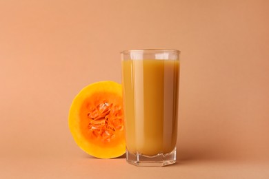 Photo of Tasty pumpkin juice in glass and cut pumpkin on pale orange background