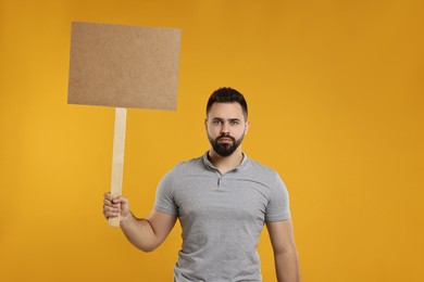Upset man holding blank sign on orange background, space for text