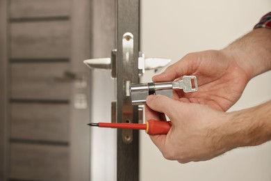 Photo of Handyman changing core of door lock indoors, closeup. Space for text