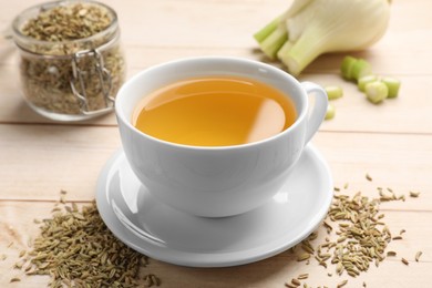 Photo of Fennel tea in cup, seeds and fresh vegetable on light wooden table, closeup