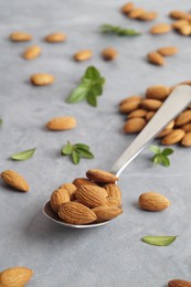 Spoon with tasty almonds and fresh green leaves on light grey table