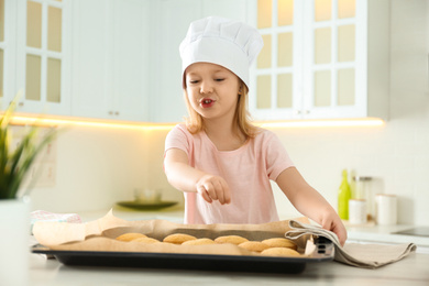 Photo of Little girl wearing chef hat baking cookies in kitchen
