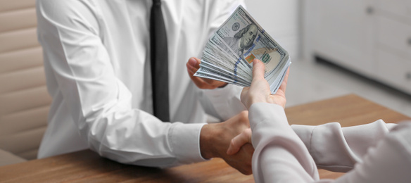 Image of Woman shaking hands with man and offering bribe at table indoors, closeup. Banner design