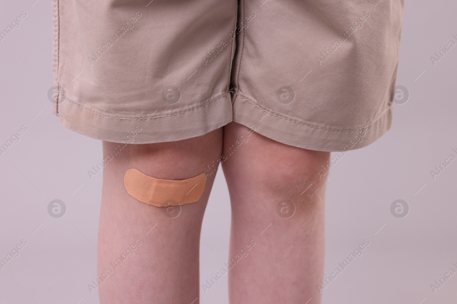 Photo of Little boy with sticking plaster on knee against light grey background, closeup