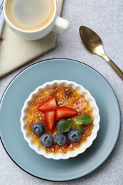 Photo of Delicious creme brulee with berries and mint in bowl served on grey textured table, flat lay