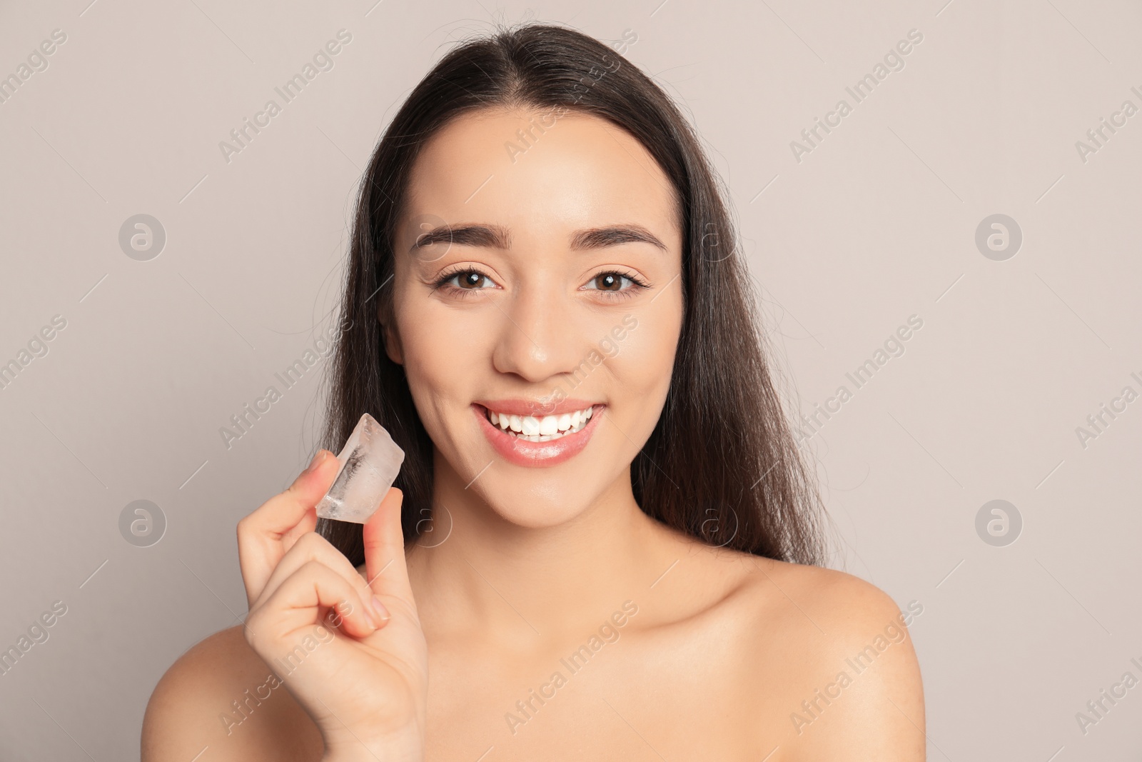 Photo of Young woman with ice cube on light background. Skin care