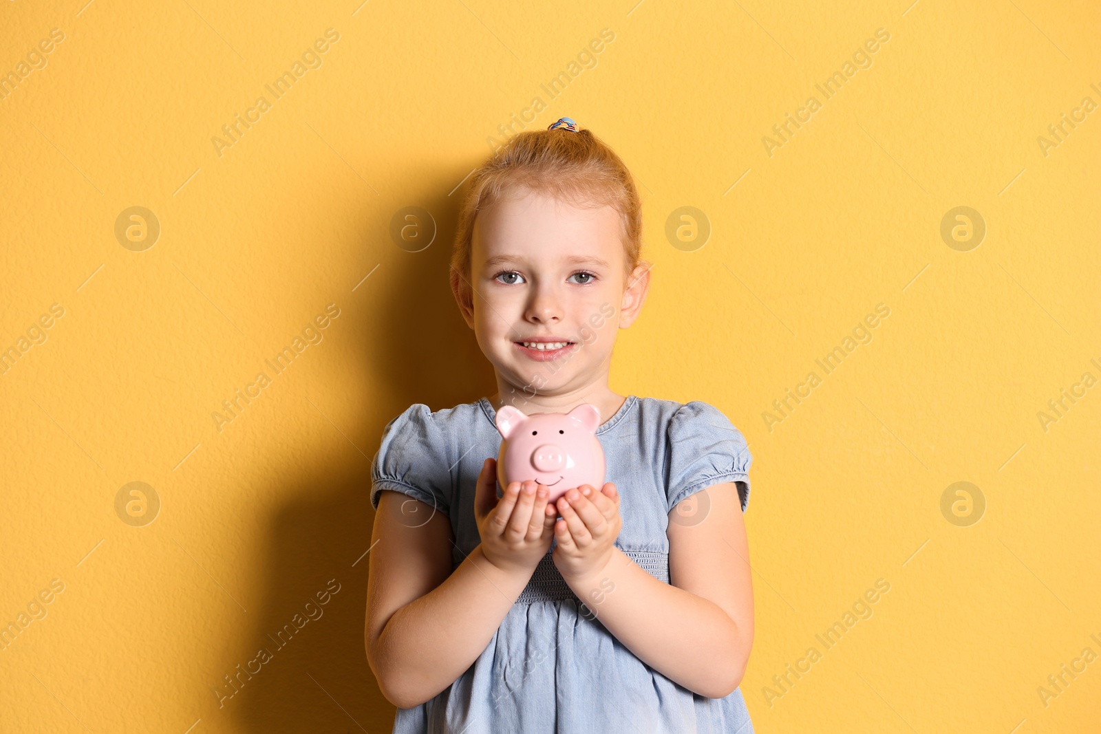 Photo of Little girl with piggy bank on color background