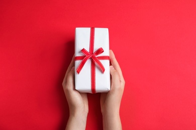 Woman holding gift box on color background, top view