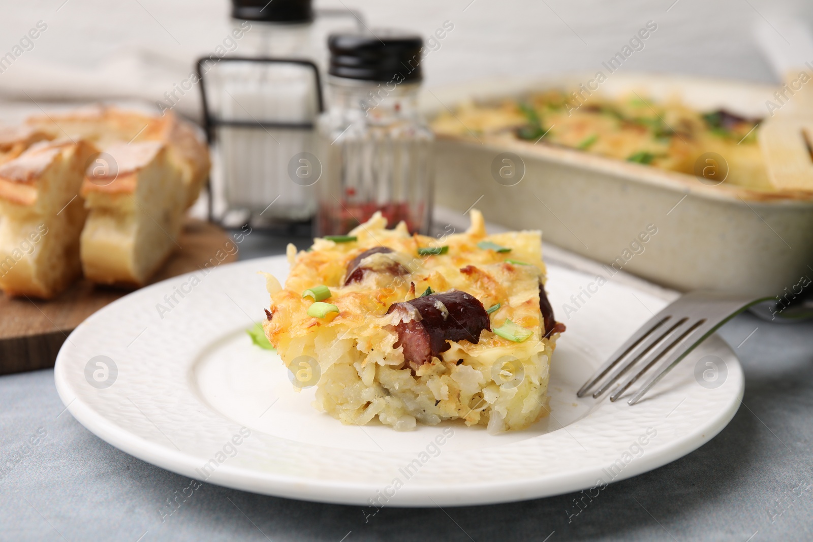 Photo of Tasty sausage casserole with green onions served on grey table, closeup