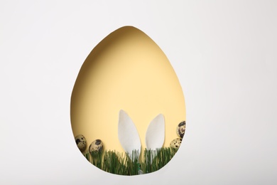 View of composition with Easter bunny ears on color background through egg shaped hole, top view. Space for text