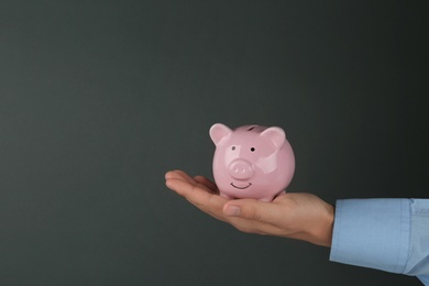 Photo of Man holding piggy bank on dark grey background, closeup view. Space for text