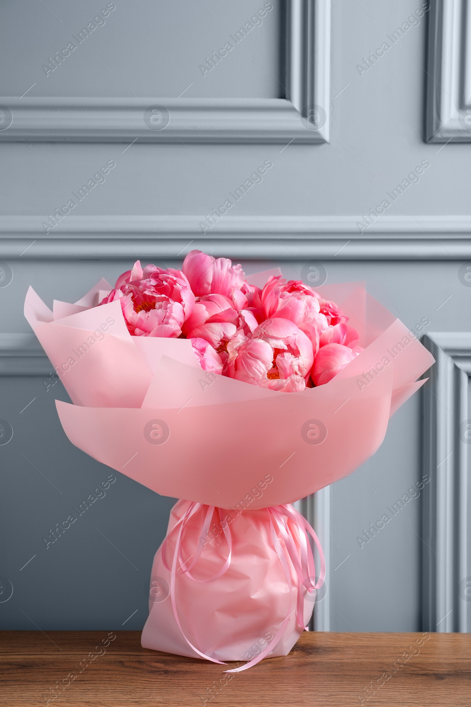 Photo of Bouquet of beautiful pink peonies on wooden table near grey wall