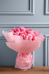 Bouquet of beautiful pink peonies on wooden table near grey wall