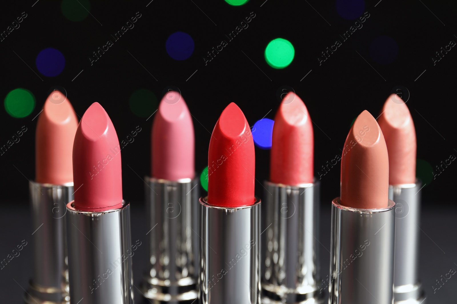 Photo of Different lipsticks against blurred lights. Cosmetic product