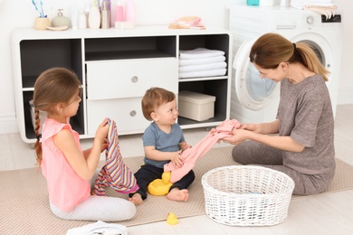 Photo of Housewife with children folding freshly washed clothes in laundry room