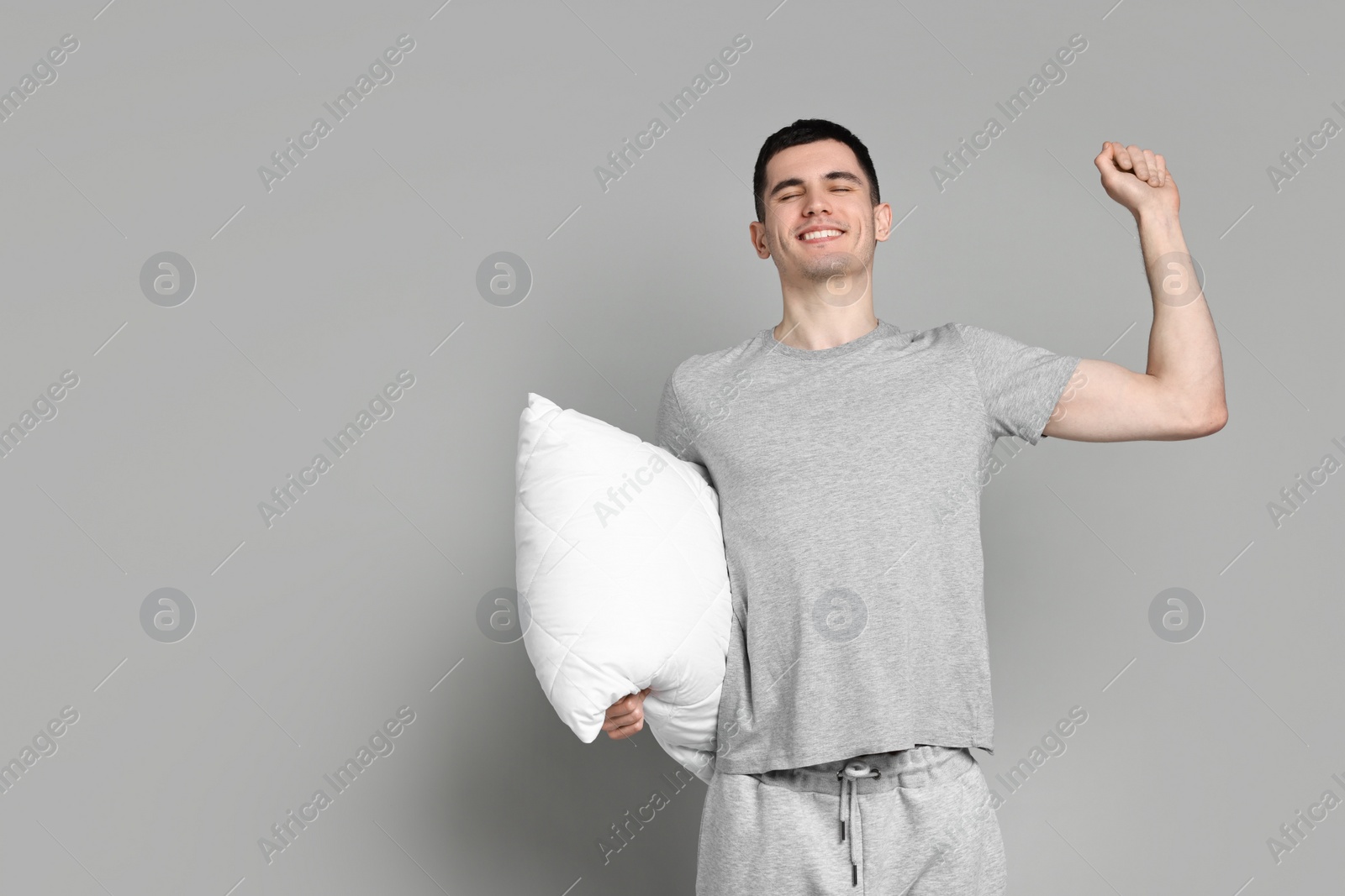 Photo of Happy man in pyjama holding pillow on grey background, space for text