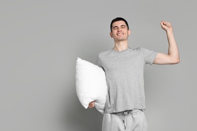 Happy man in pyjama holding pillow on grey background, space for text