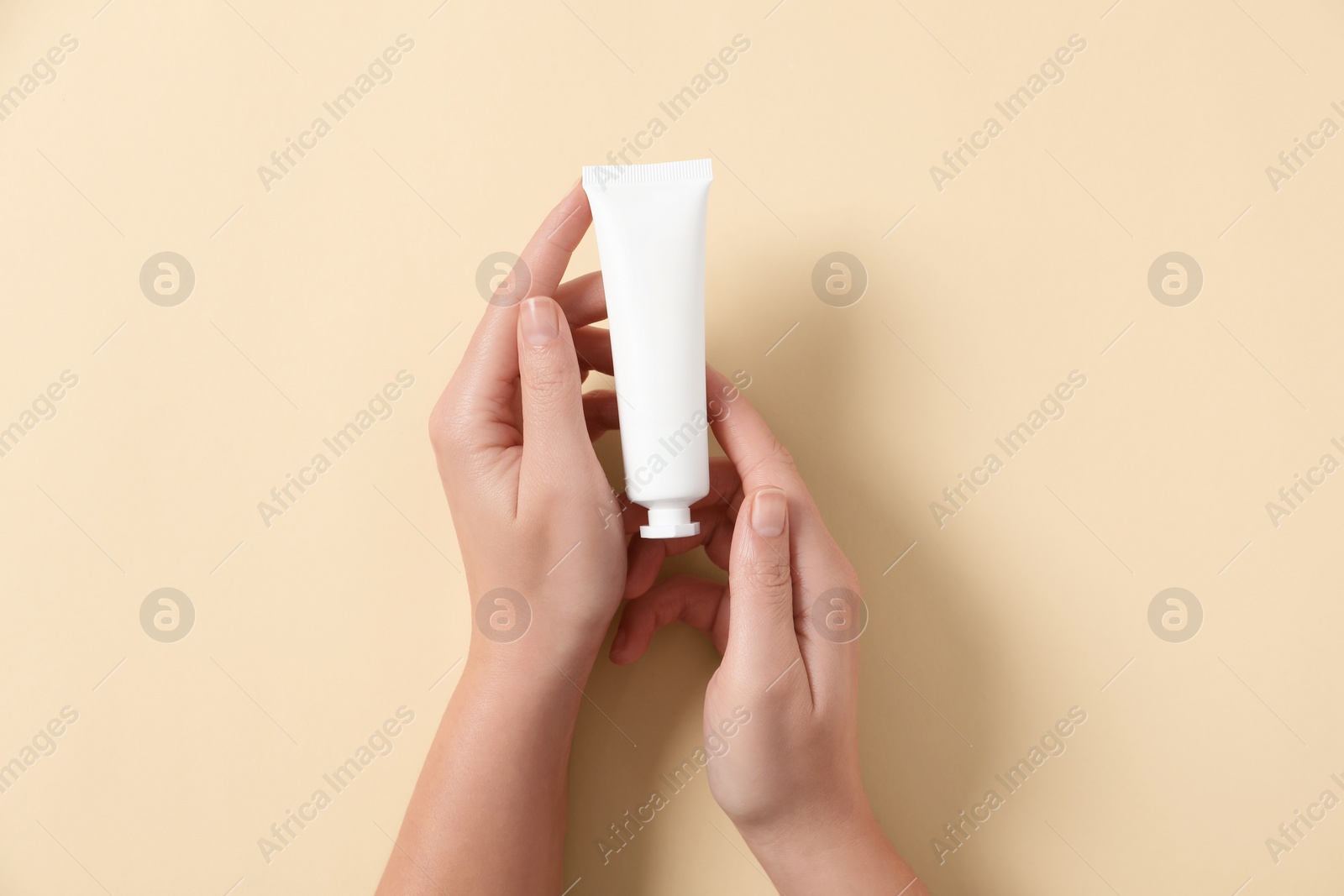 Photo of Woman with tube of hand cream on beige background, top view