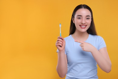 Happy young woman holding plastic toothbrush on yellow background, space for text
