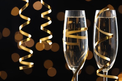 Glasses of champagne and serpentine streamers against black background with blurred lights, closeup. Space for text