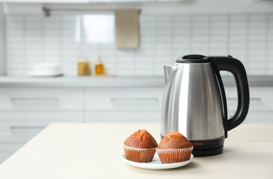 Photo of Modern electric kettle and muffins on wooden table in kitchen. Space for text