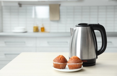 Modern electric kettle and muffins on wooden table in kitchen. Space for text