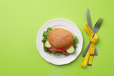 Tasty sandwich and cutlery tied with  measuring tape on color background, top view. Healthy diet