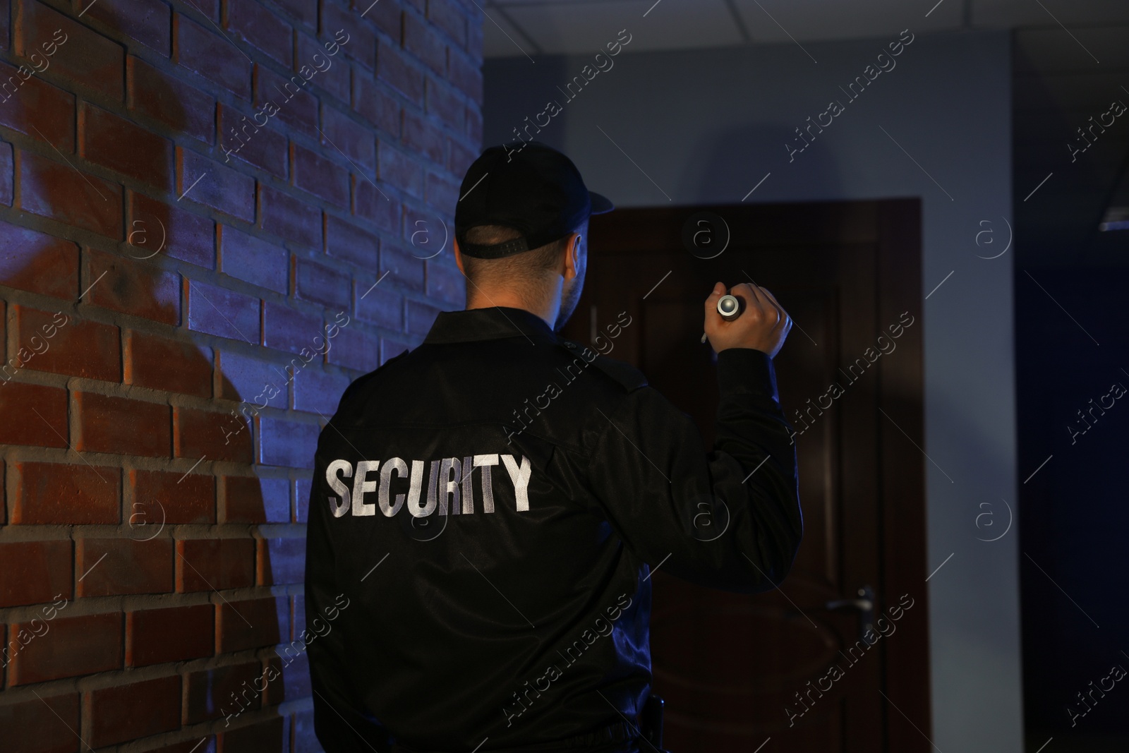 Photo of Male security guard with flashlight in dark corridor