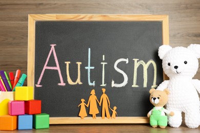 Photo of Chalkboard with word Autism, paper cutout of family and different toys on wooden table